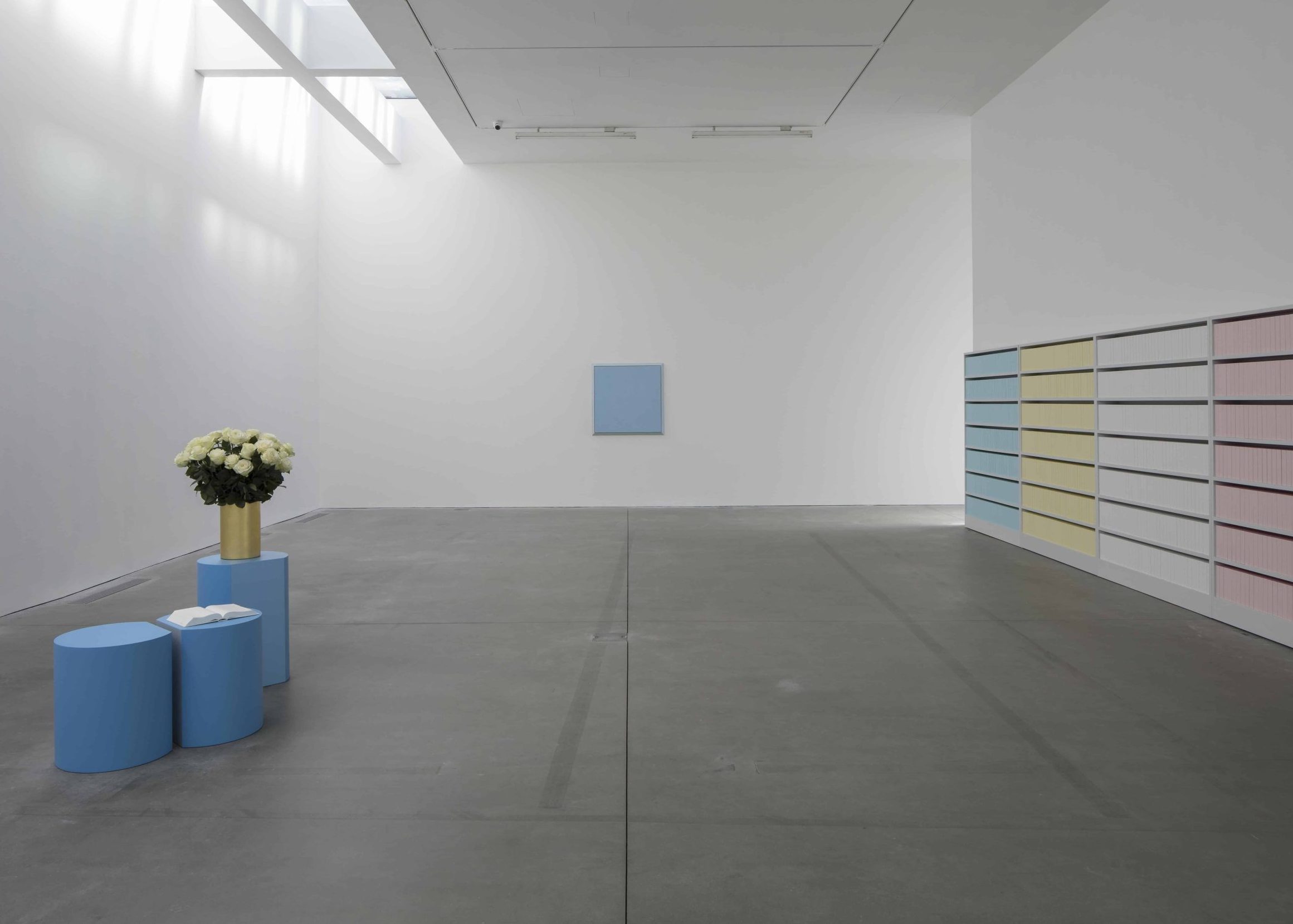 Minimalist gallery with blue, yellow and pink panels on the right for art for enterprise, blue tables with white roses on the left and a small blue square.